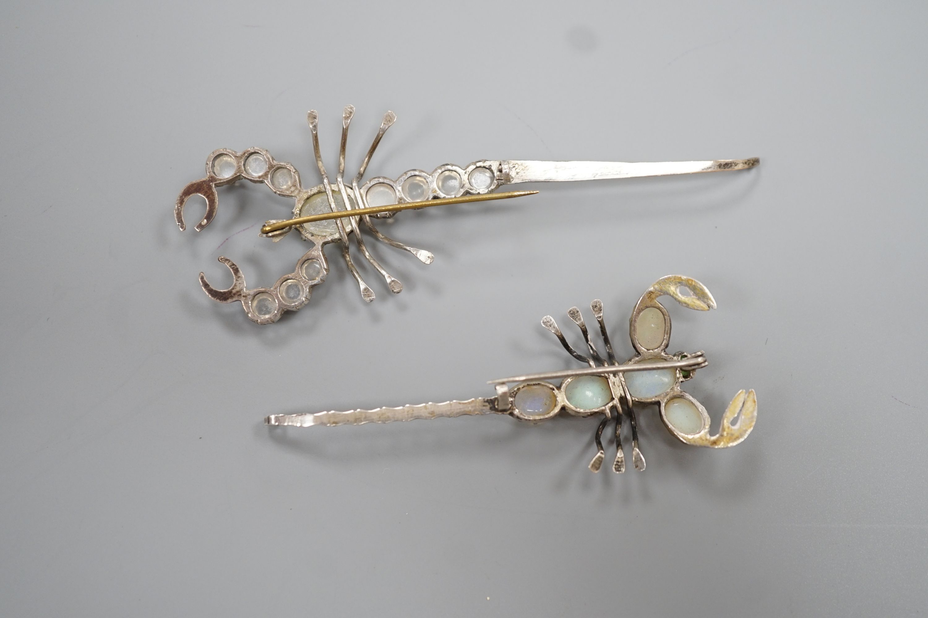 Two white metal scorpion brooches, one set with moonstones, the other with opals, largest 9cm.